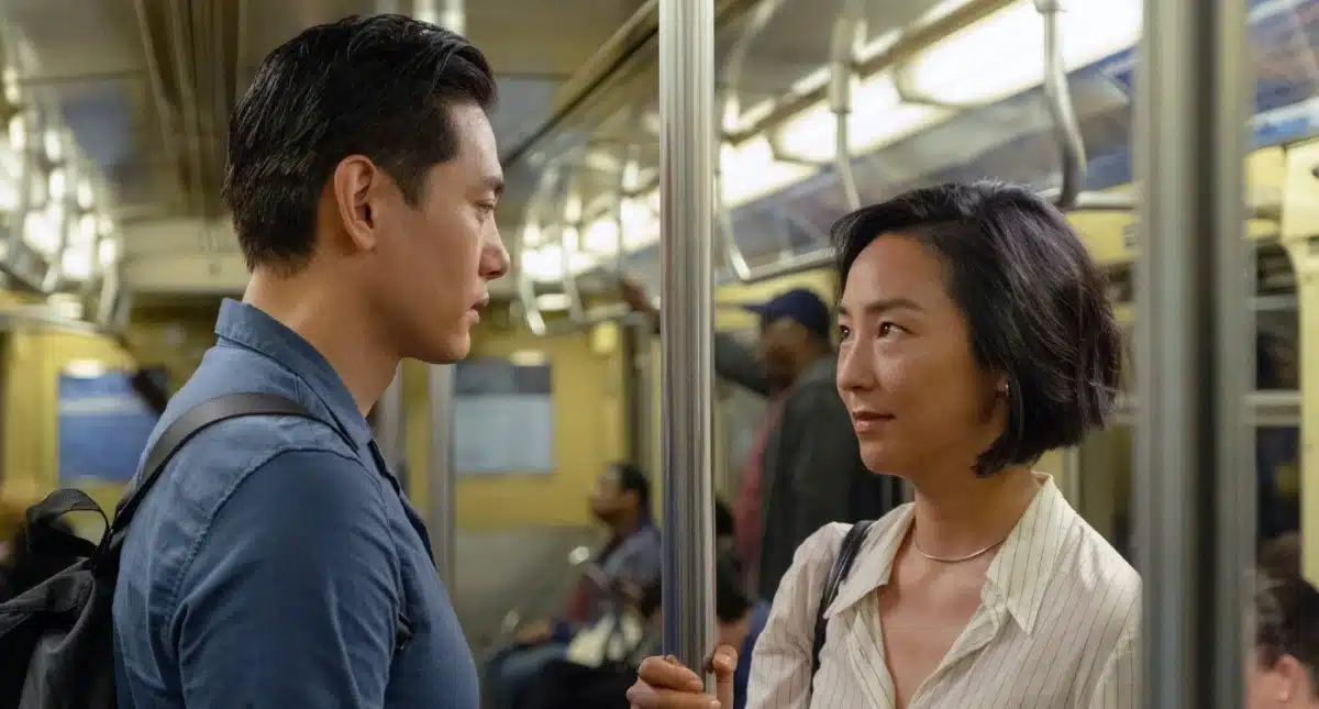 Still from the movie Past Lives. An adult man and an adult woman look longingly at each other on a subway train