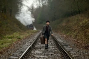 Boy in the film Blitz walks along train tracks, holding a suitcase.