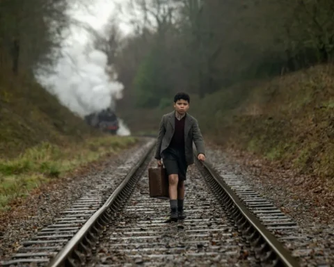 Boy in the film Blitz walks along train tracks, holding a suitcase.