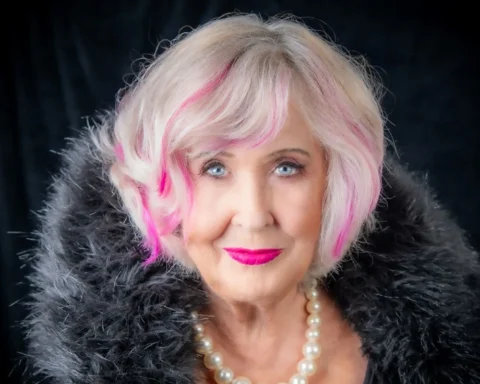 Woman over 50 with pink hair smiles at camera.