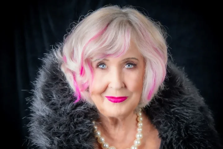 Woman over 50 with pink hair smiles at camera.