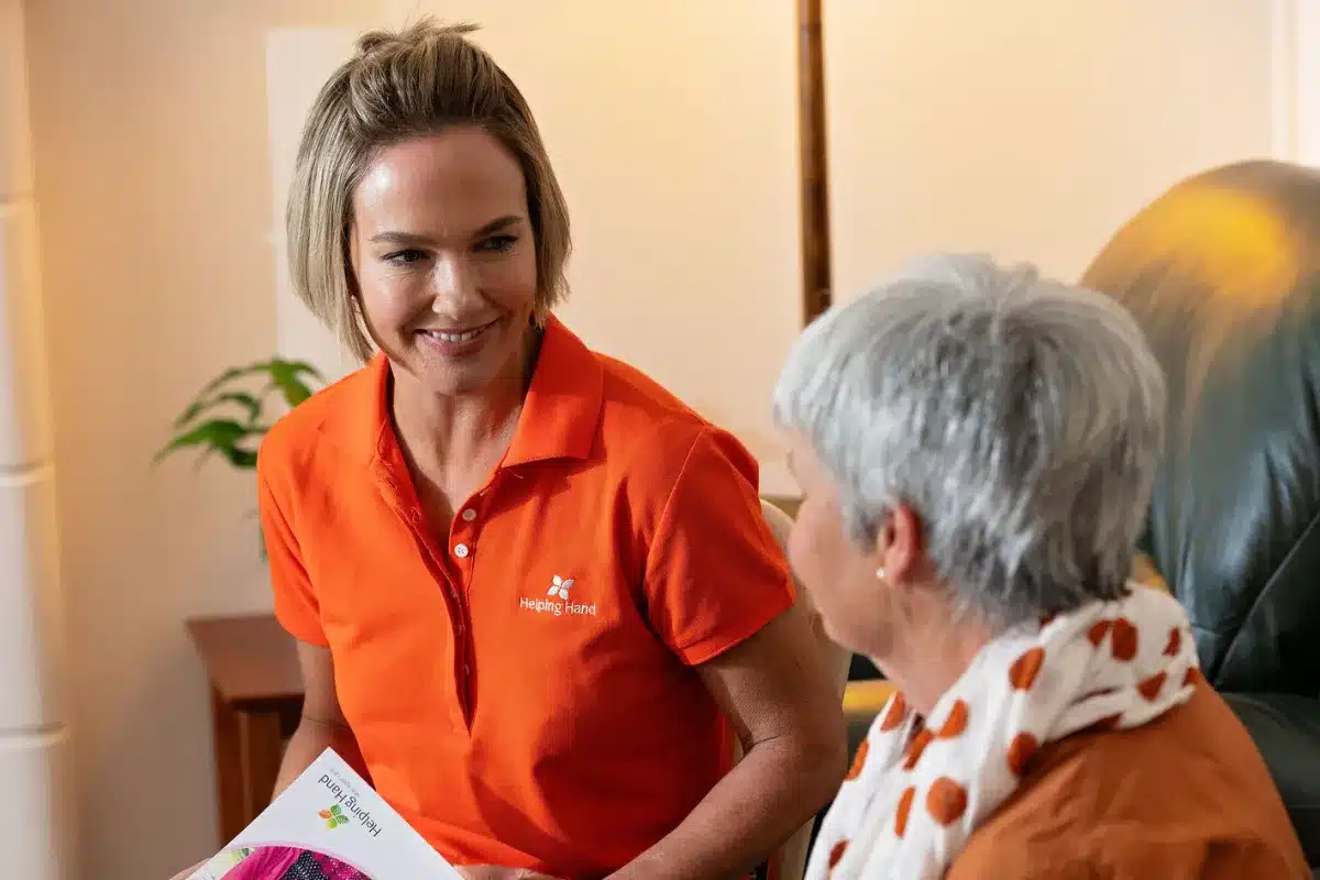 A woman in an orange shirt engages in conversation with an older woman, sharing a moment of connection.