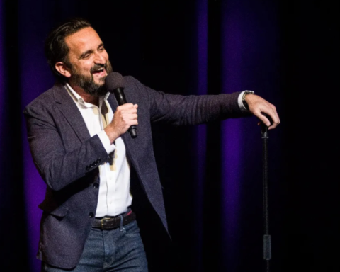 Comedian, Sami Shah on stage with microphone.