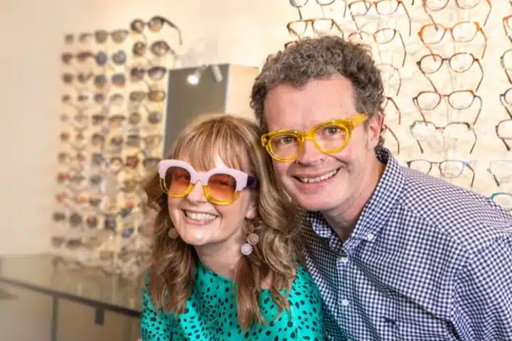 In a store, a man and woman with glasses are seen together, actively shopping and reviewing items on display.