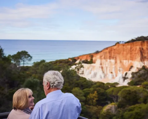 Older couple stare lovingly at each other with beach landscape in the distant.