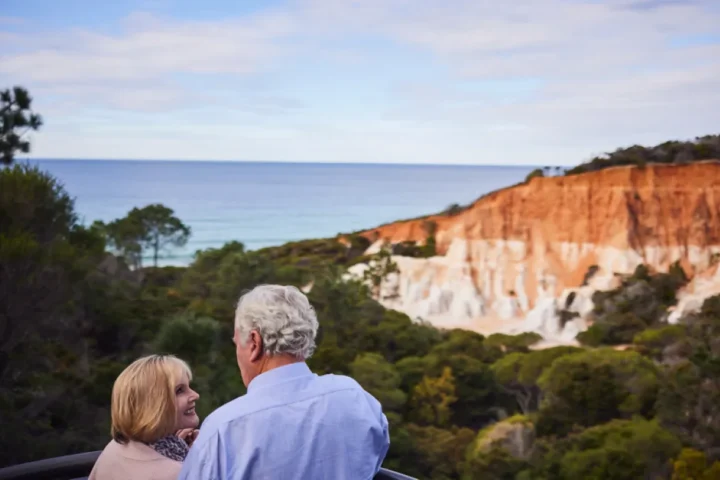 Older couple stare lovingly at each other with beach landscape in the distant.