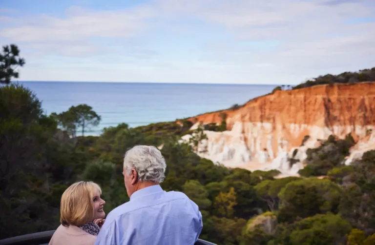 Older couple stare lovingly at each other with beach landscape in the distant.