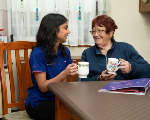 A woman and an older woman sit together at a table, enjoying cups of tea.