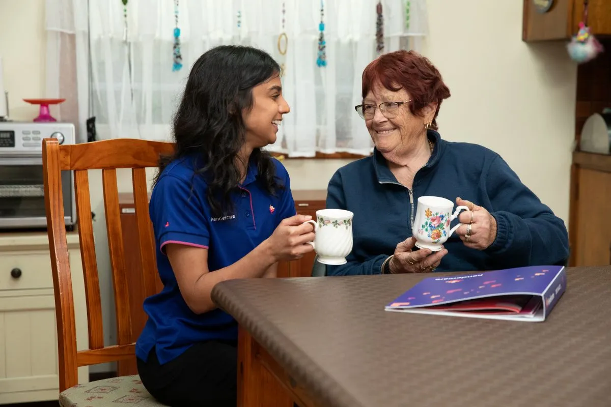 A woman and an older woman sit together at a table, enjoying cups of tea.