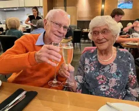 An elderly couple toasting with champagne glasses at a restaurant.