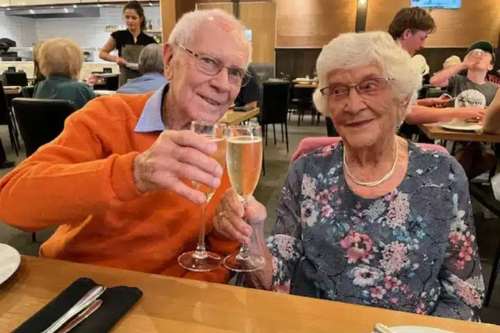 An elderly couple toasting with champagne glasses at a restaurant.