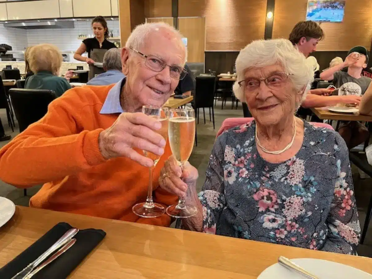 An elderly couple toasting with champagne glasses at a restaurant.