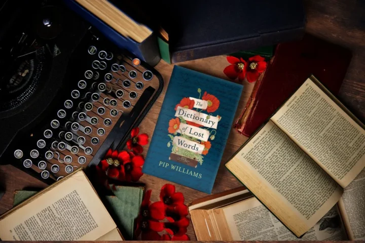 A typewriter, stacked books, and a bouquet of flowers elegantly arranged on a wooden table.