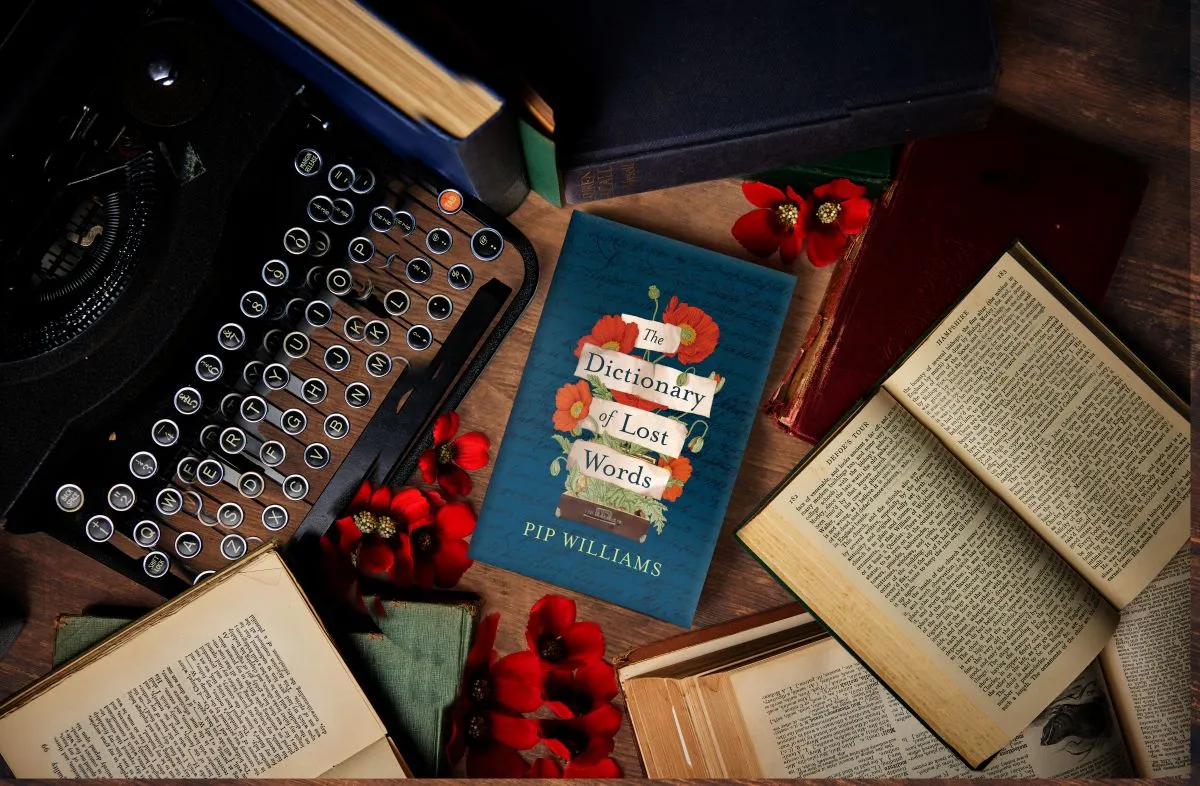 A typewriter, stacked books, and a bouquet of flowers elegantly arranged on a wooden table.