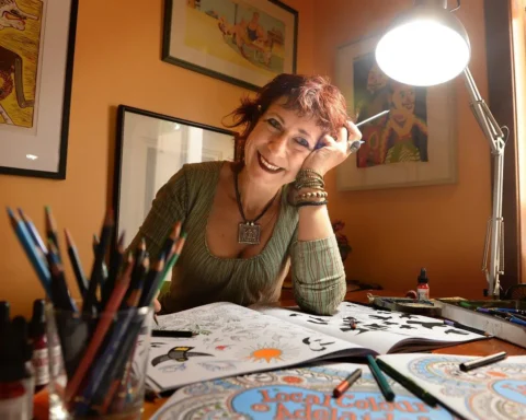 A woman smiles as she draws on a table, showcasing her creativity and joy in the artistic process.