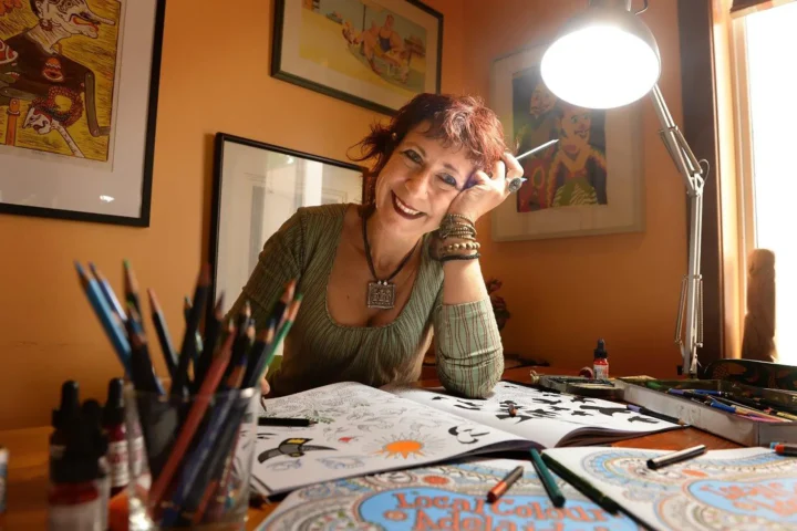 A woman smiles as she draws on a table, showcasing her creativity and joy in the artistic process.