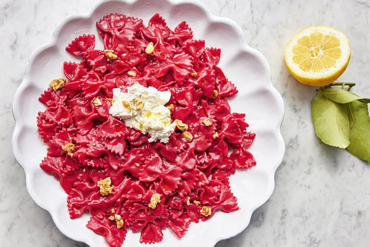 A plate of vibrant red pasta garnished with lemon slices and sprinkled with walnuts, creating a colourful dish.