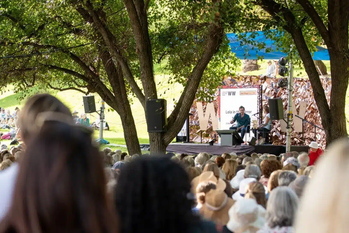 A large crowd of people stands together, eagerly watching a performance on a stage.