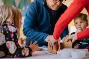 A man and woman assist children in constructing colorful gingerbread houses during a festive activity.