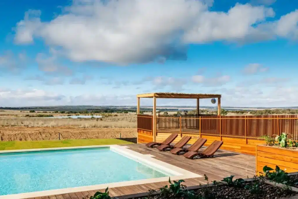 A wooden deck surrounds a pool, offering a scenic view of the lush countryside in the background.