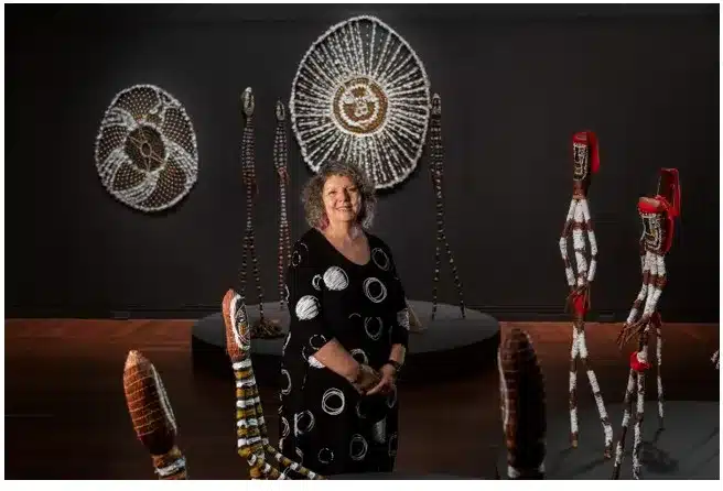 A woman stands in front of a vibrant display showcasing various pieces of native art.