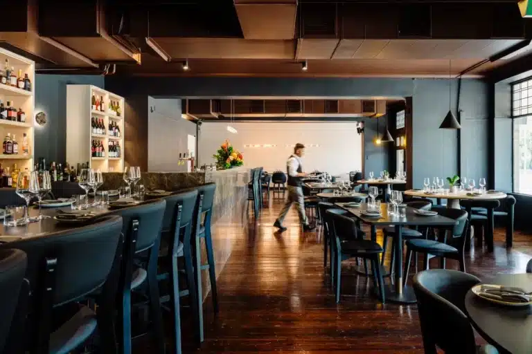 A cozy restaurant interior featuring tables, chairs, and a well-stocked bar for dining and socializing.