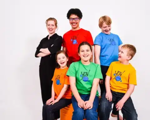 A group of smiling children in bright, colorful shirts posing together for a cheerful photo.