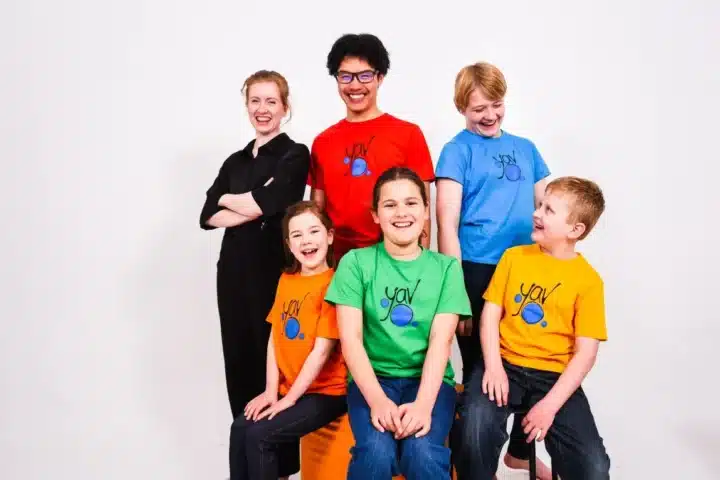 A group of smiling children in bright, colorful shirts posing together for a cheerful photo.