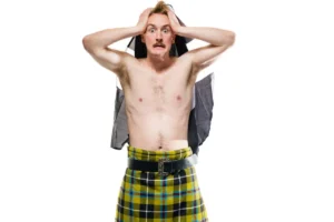 A man in a kilt stands with his head held in his hands, expressing a moment of contemplation or distress.