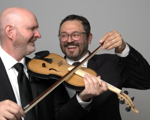 Two men in formal suits and ties are holding a violin, showcasing a blend of elegance and musical artistry.