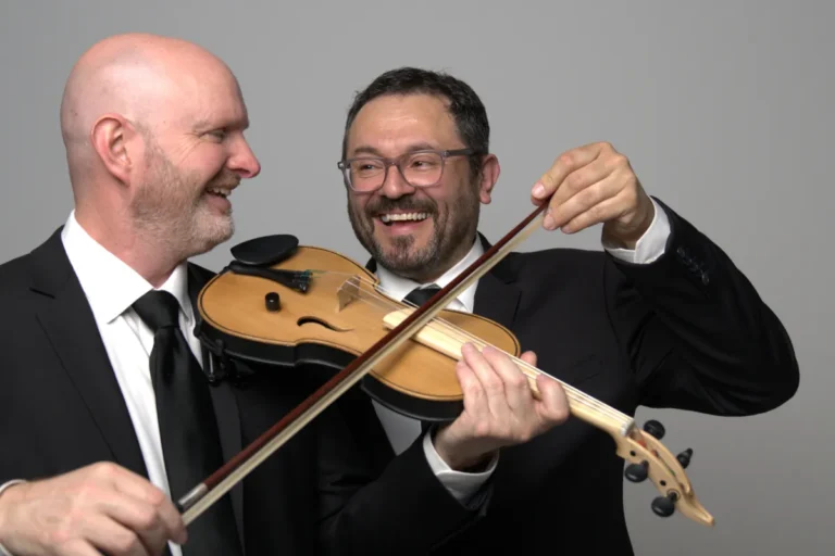 Two men in formal suits and ties are holding a violin, showcasing a blend of elegance and musical artistry.