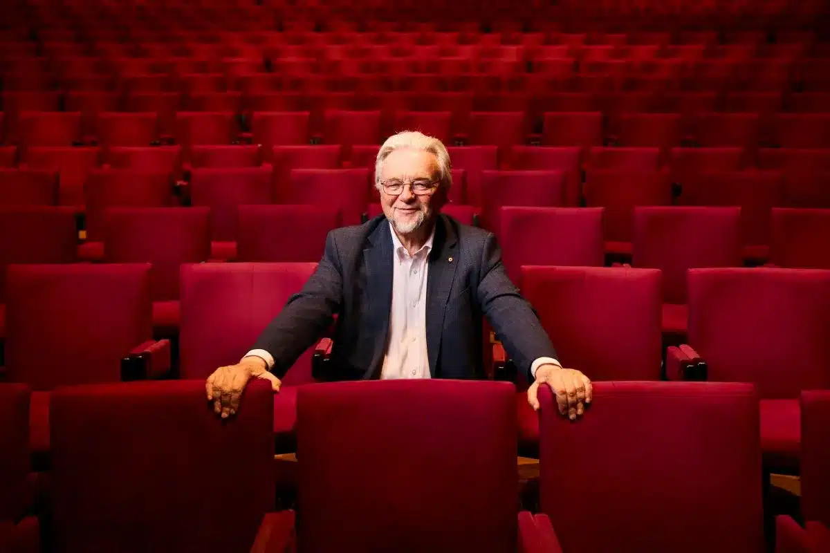 A man with crossed arms sits in a red auditorium, surrounded by plush red seats and a vibrant atmosphere.