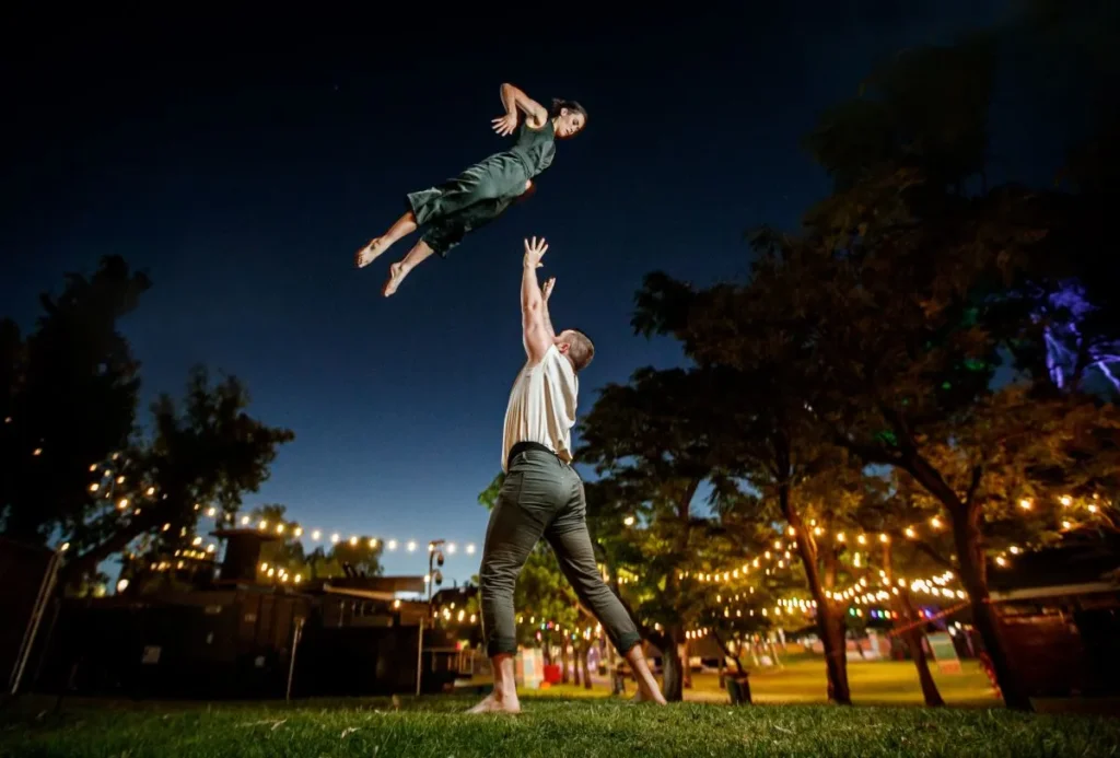 A man and woman soaring through the night sky, illuminated by stars and moonlight.