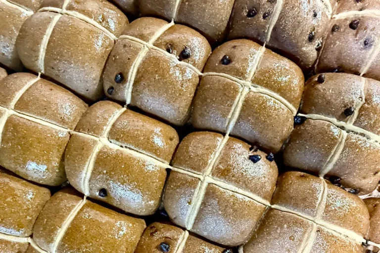 A stack of warm chocolate chip hot cross buns, freshly baked and golden brown, ready to be enjoyed.