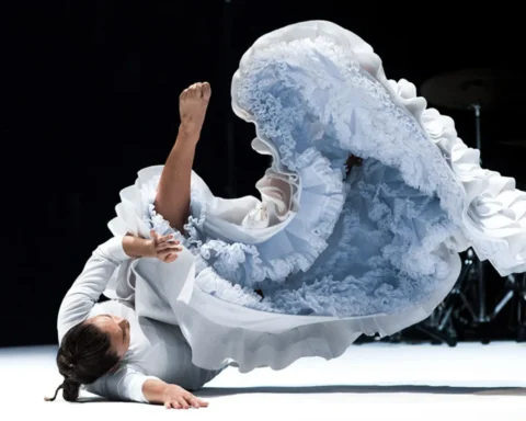 A woman in a white dress gracefully performs on stage, captivating the audience with her presence and talent.