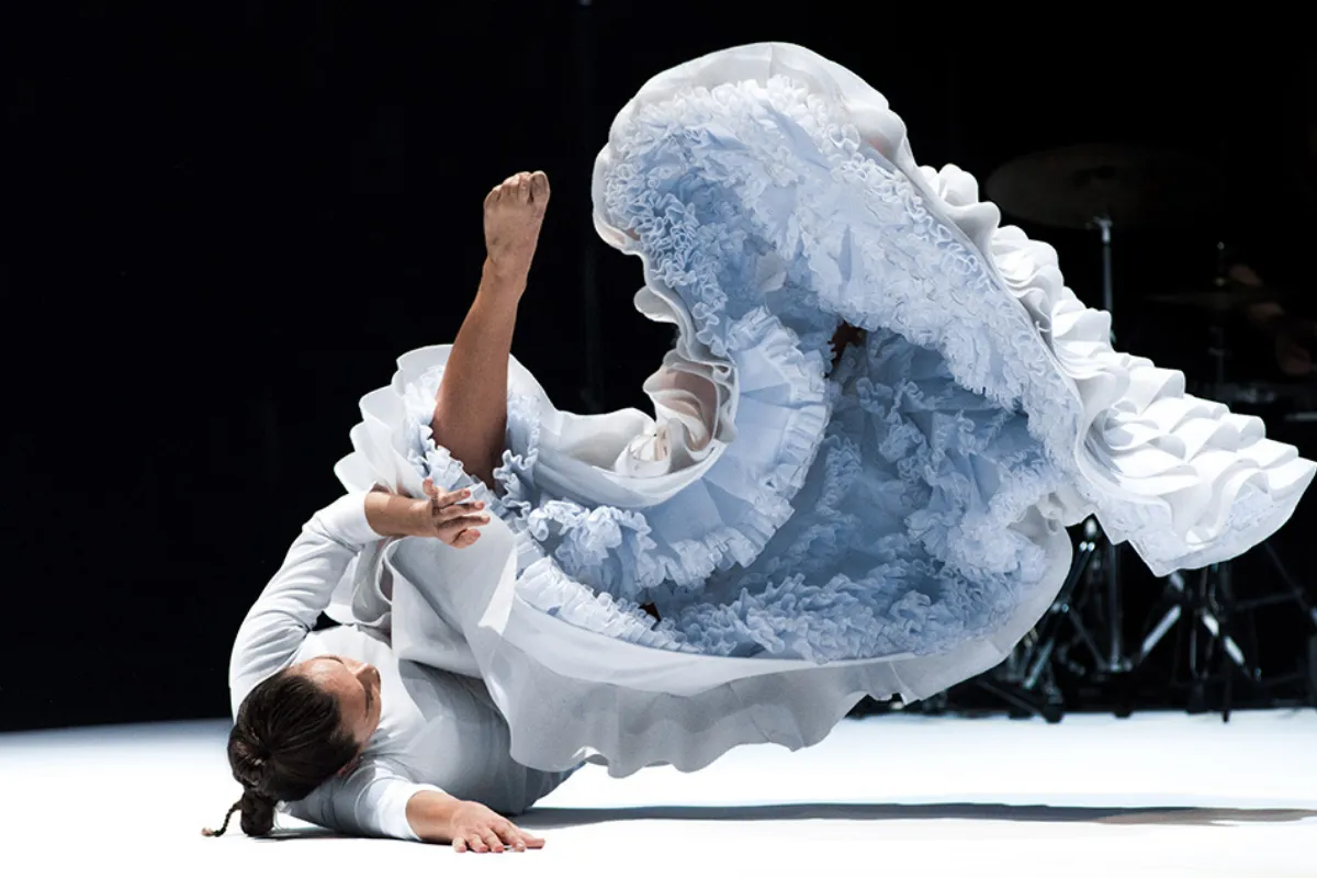 A woman in a white dress gracefully performs on stage, captivating the audience with her presence and talent.