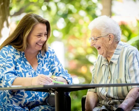 A woman and an older woman are seated at a table, reviewing documents together with focused expressions.