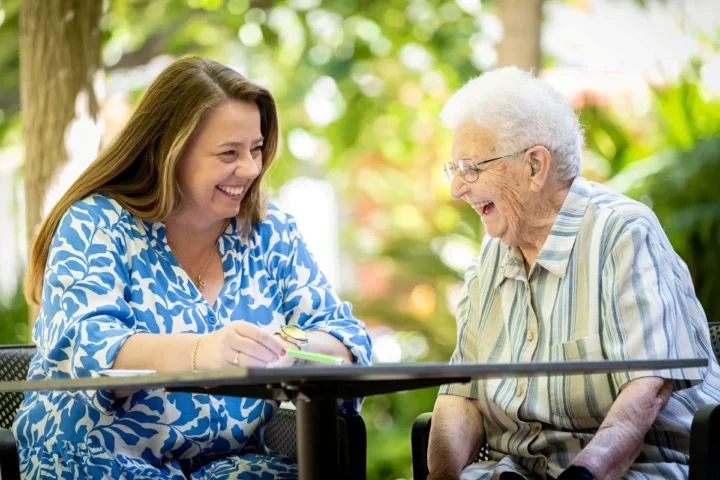 A woman and an older woman are seated at a table, reviewing documents together with focused expressions.