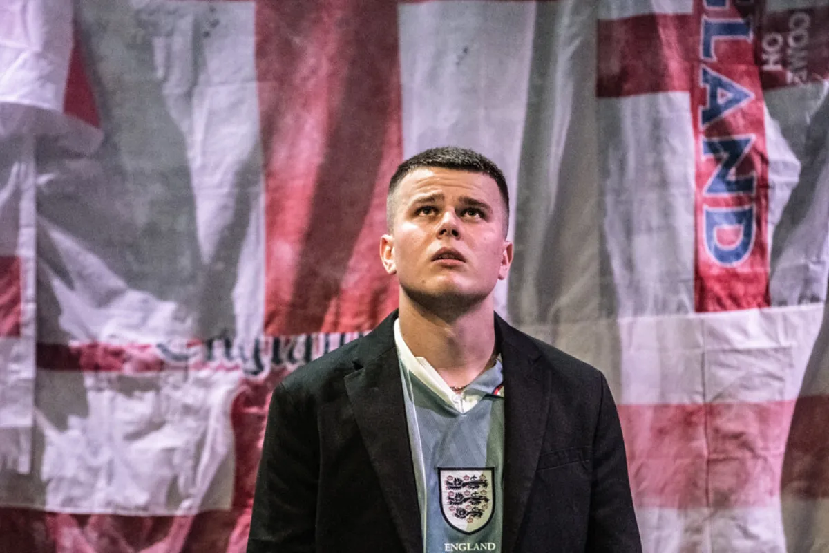 A man in a suit stands confidently in front of a large flag, showcasing professionalism and patriotism.