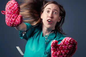 A woman in a green scrub suit is holding two oven mitts, ready to handle hot dishes with care and safety.