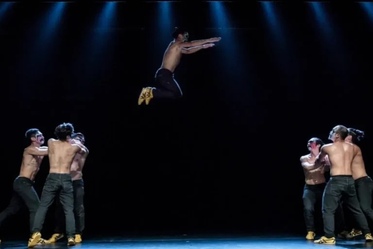 A group of men performing acrobatics in mid-air on a stage, showcasing their skills and teamwork.