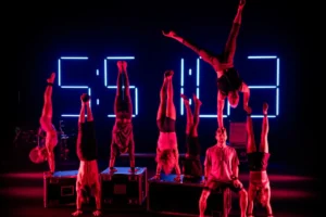 A vibrant stage performance featuring a group of people illuminated by colorful neon lights.