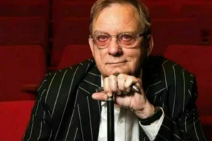 A man wearing glasses and a pinstripe suit sits comfortably in a vibrant red chair.