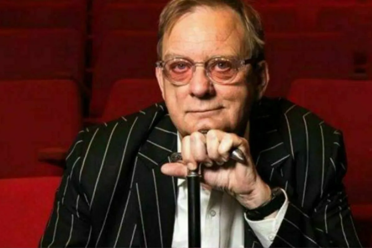 A man wearing glasses and a pinstripe suit sits comfortably in a vibrant red chair.