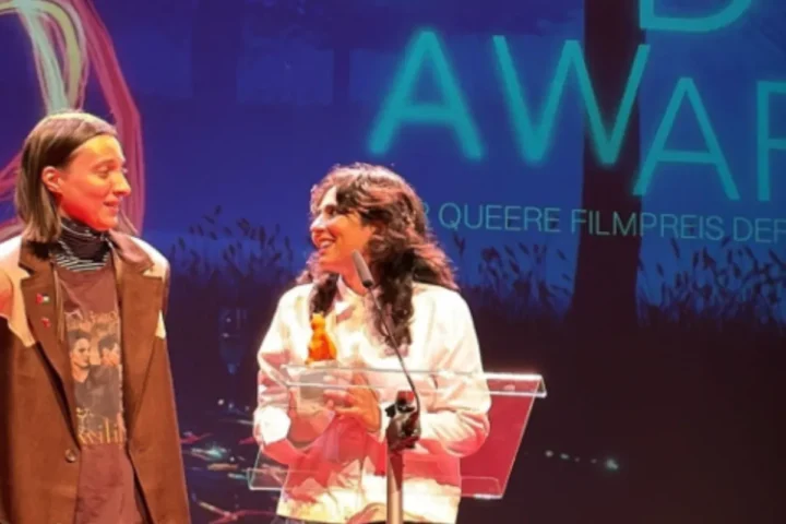 Two individuals on stage proudly holding an award, celebrating their achievement in front of an audience.