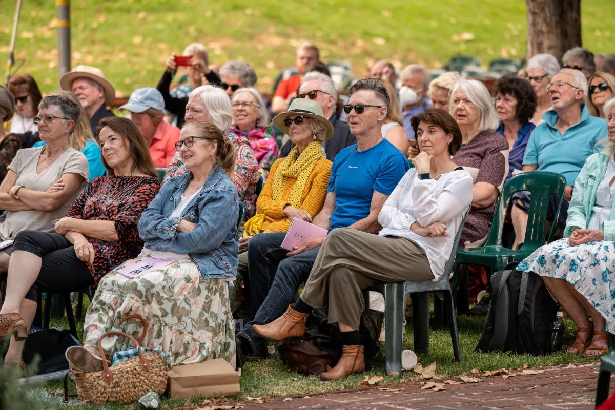 A diverse crowd of people seated in chairs, enjoying an outdoor event under a clear sky.