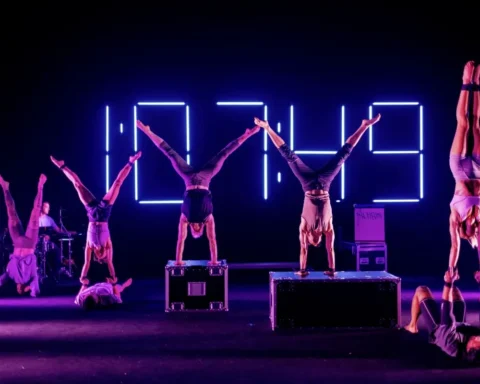 A group of acrobats performing on stage, showcasing their skills with a large clock in the background.