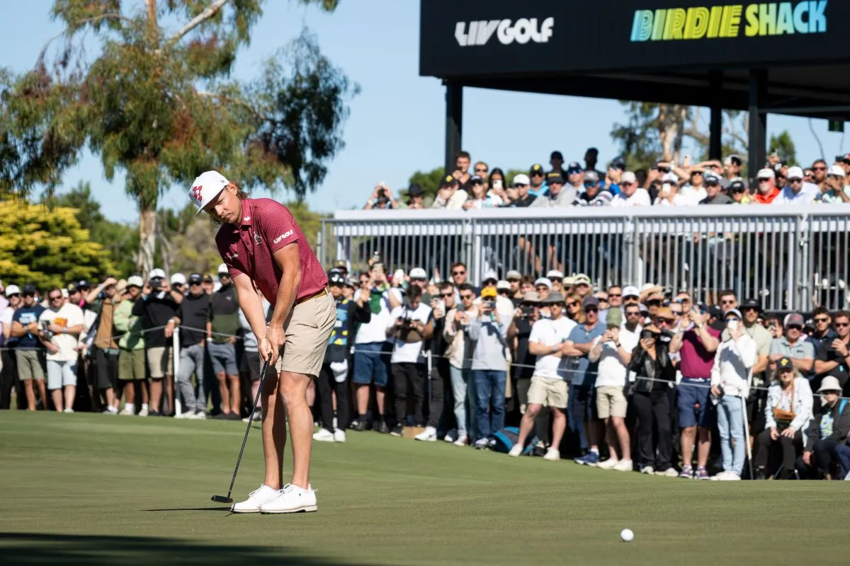 A man in a red shirt and white pants is putting on the green during a golf game.