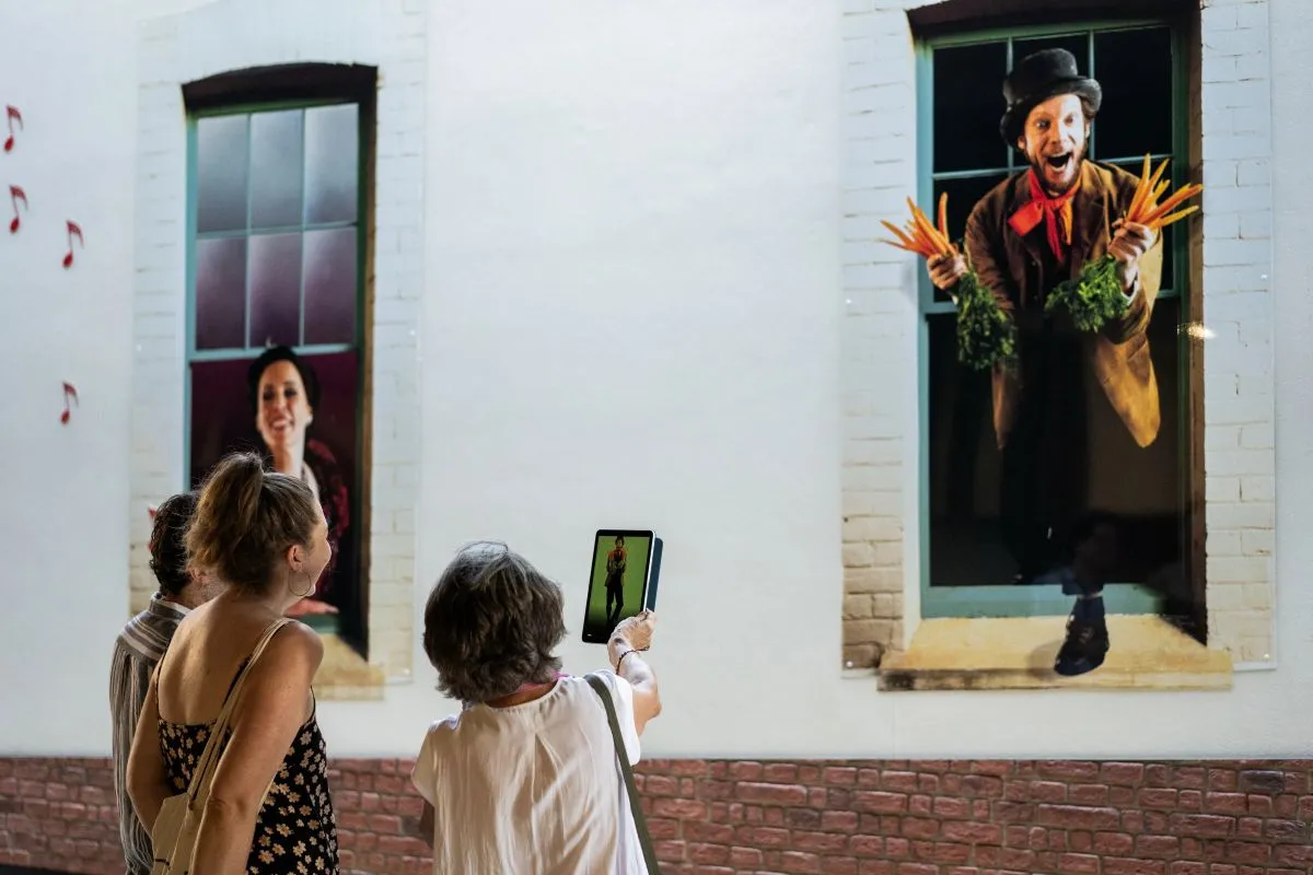 A group of people capturing photos of a painting depicting a man looking out from a window.