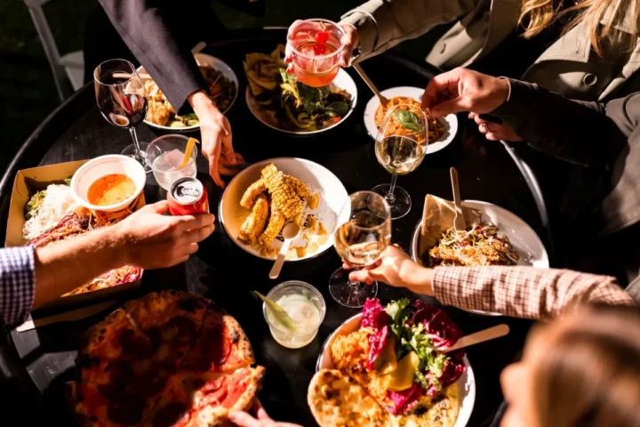 A group of friends joyfully toasting with glasses of wine while enjoying a delicious spread of food together.